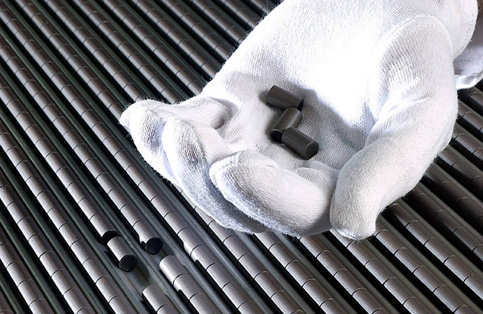 Uranium fuel pellets held in a gloved hand over fuel rods