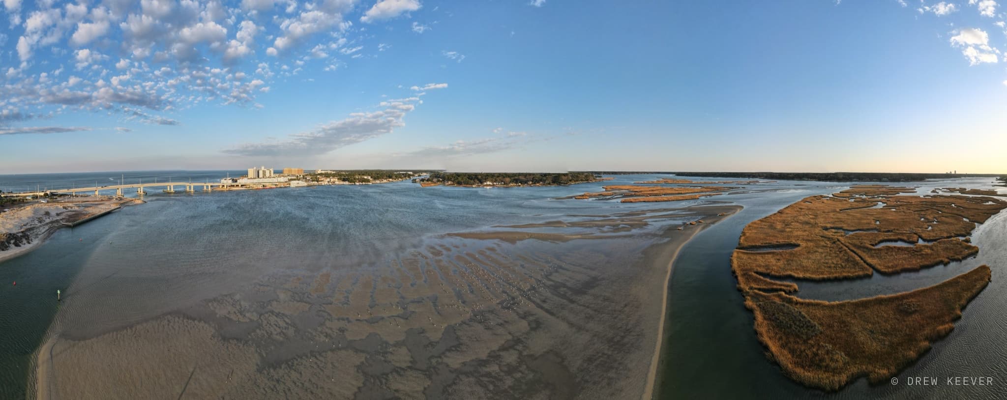 Aerial winter panorama of sandbars and shoals exposed at low tide, with a flock of birds resting on the flats and the Lesner Bridge in the distance