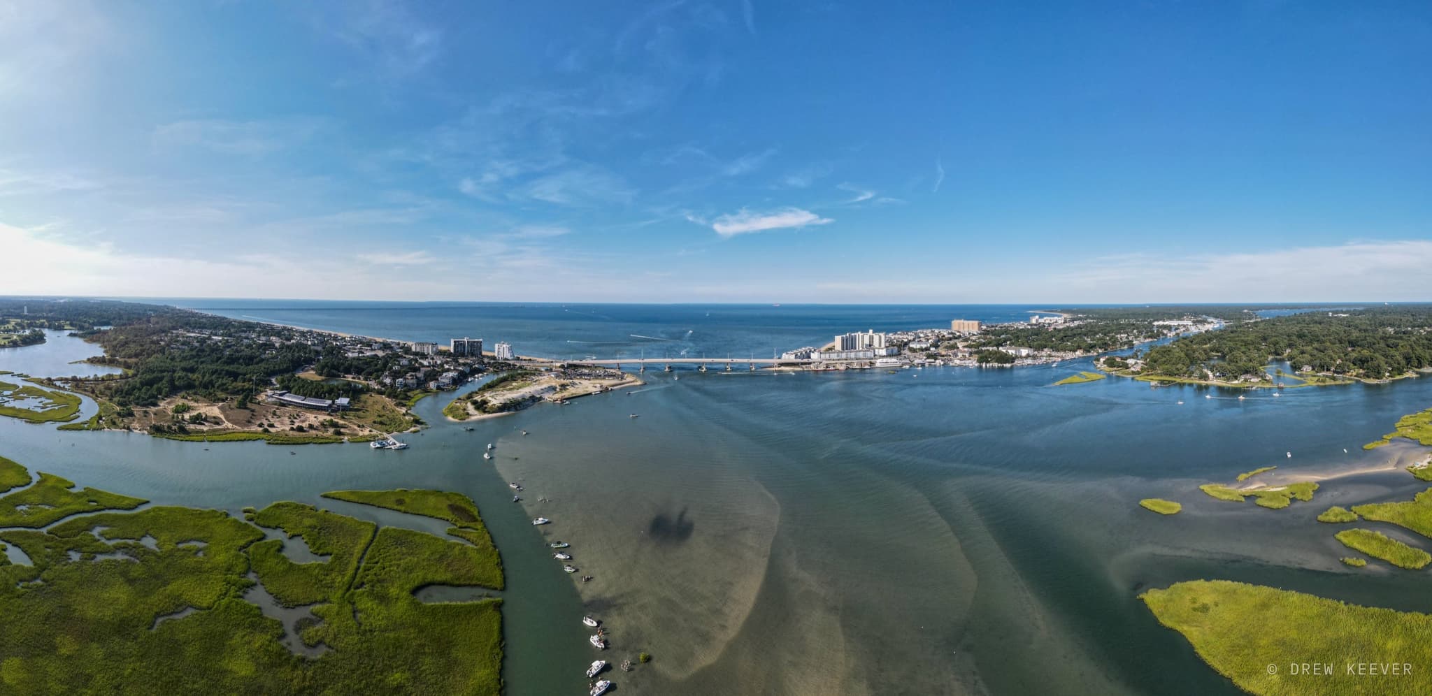 Aerial summer panorama of the Lynnhaven Inlet, where the river channel and green salt marsh meet the Chesapeake Bay under a blue sky
