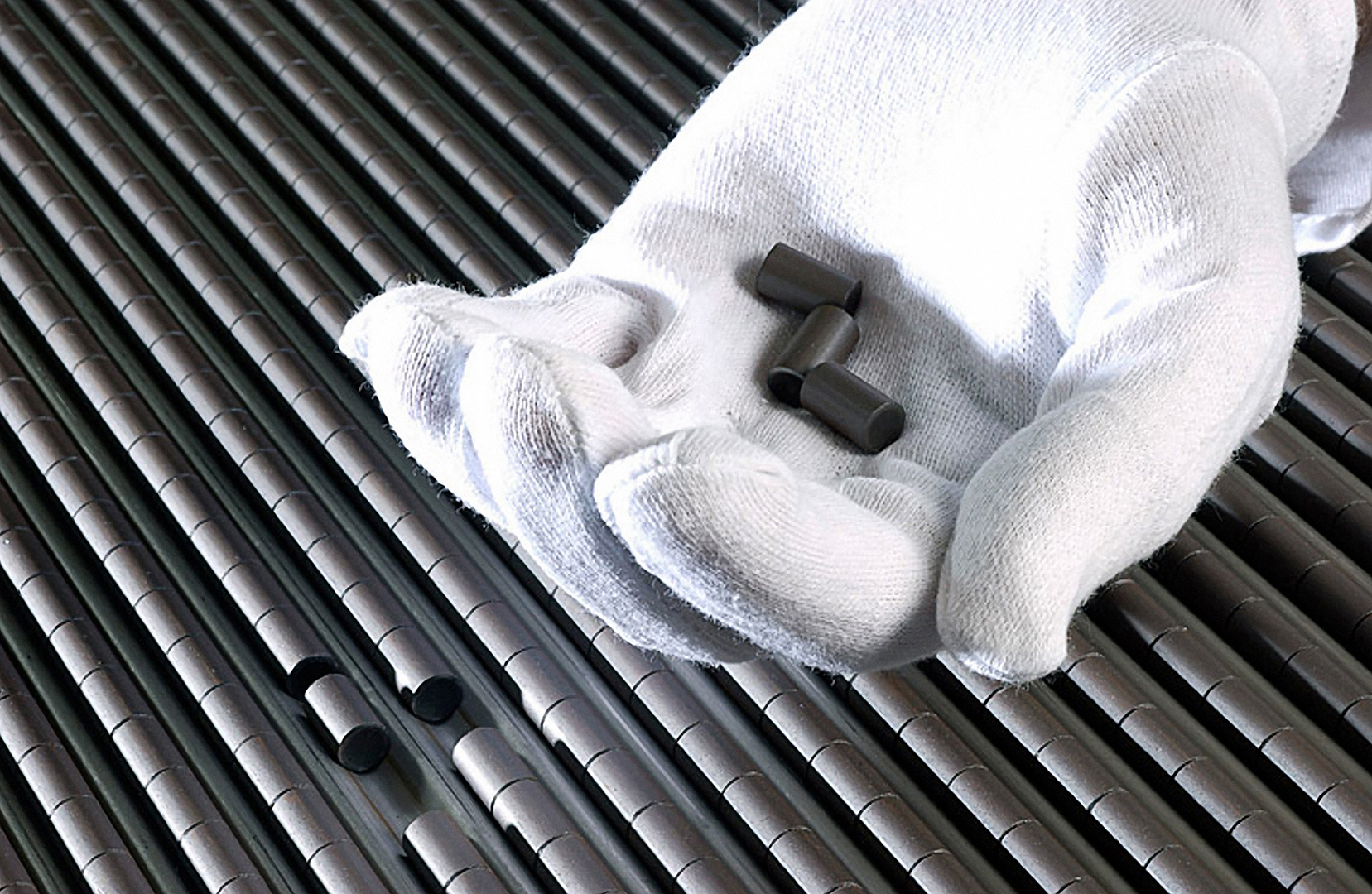 Uranium fuel pellets held in a gloved hand over fuel rods